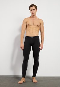 Melnas leggingas, izgatavotas no elastīga auduma, ar pieguļošu dizainu, elastīgu jostu un gludu struktūru. Nav redzamu rakstu vai akcentu.