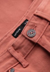 Baumwollhemd in staubigem Rosé mit strukturiertem Finish, ausgestattet mit einem Knopf und einem Etikett. Enthält eine Schlaufe zum Aufhängen.
