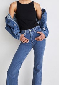 Black sleeveless top paired with a light blue denim jacket and high-waisted blue jeans, featuring classic five-pocket design and minimal distressing.