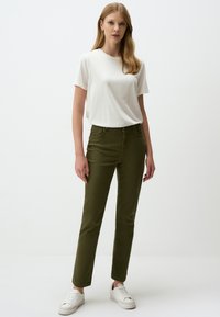 Groene katoenen broek met een slanke pasvorm, ritssluiting en vijf zakken, gecombineerd met een wit T-shirt met ronde hals en witte sneakers.