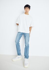 Camiseta blanca de gran tamaño, jeans de color azul claro y zapatillas Nike grises. Líneas limpias, ajuste casual y tejido texturizado. Diseño minimalista sin patrones.