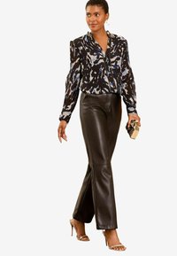 Zwarte en blauwe blouse met een patroon en pofmouwen, gecombineerd met hoge zwarte leren broeken en gespsandalen met hoge hakken. Gouden clutch.