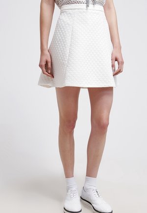 Jupe blanche matelassée avec une forme évasée en A, présentant une texture lisse et une taille haute. Associée à des chaussures et des chaussettes blanches.