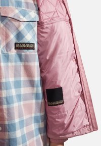 Prošívaný růžový rukáv bundy s hladkou texturou; kostkovaná modro-růžová košile s náprsní kapsou. Značkové štítky na obou oděvech.