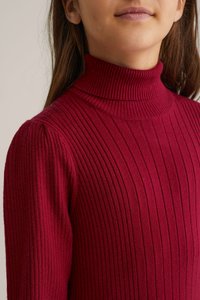 Rdeča rebrasta turtleneck majica s fitted obliko, ki vključuje vertikalne črte in visok ovratnik. Na tkanini je vidna mehak tekstura.