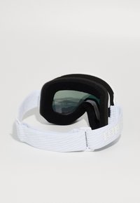 Baltie slēpošanas brillēm ar zaļiem stikliem, mīkstu melnu polsterējumu un teksturētu baltu siksnu ar logo. Ergonomiski izstrādātas komfortam.