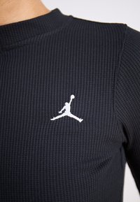 Fekete bordás hosszúujjú felső, bal mellen fehér Jumpman logóval, magas nyakkivágással és texturált anyaggal.