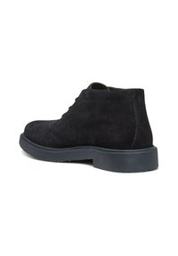 Stivali alla caviglia in suede nero con punta arrotondata, suola in gomma bassa e dettagli di cucitura discreti. La parte superiore ha una texture liscia e un design minimalista.