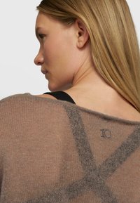 Brązowy sweter dzianinowy o luźnym kroju, z krzyżującym się wzorem i małym haftem "10" na plecach.