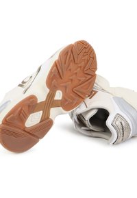 Zapatillas deportivas blancas con un upper texturizado, detalles plateados y una suela de goma con un patrón de tracción multidireccional.