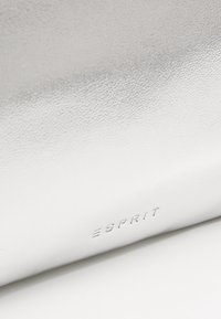 Pochette synthétique texturée argentée avec logo "ESPRIT" en relief, présentant une surface lisse et une l égère brillance.