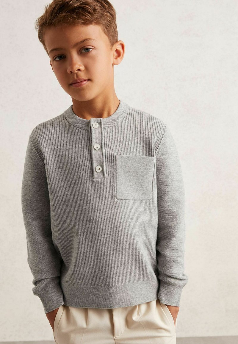 Camisa de manga larga gris acanalada con cuello henley, tres botones y un bolsillo de parche. Textura suave y diseño ajustado.