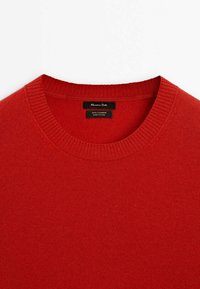 Pull en cachemire rouge à col rond avec col côtelé, avec une étiquette noire indiquant la marque et les détails du matériau.