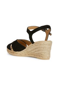 Sandalo con zeppa in suede nero, con tacco in juta intrecciata, caratterizzato da cinturini incrociati e una cinghia alla caviglia posteriore per un supporto aggiuntivo.