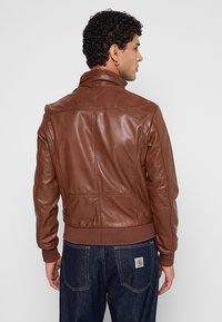 Bruine leren bomberjack met een geribde zoom en manchet, voorzien van een gladde textuur en stikdetails op de rug.