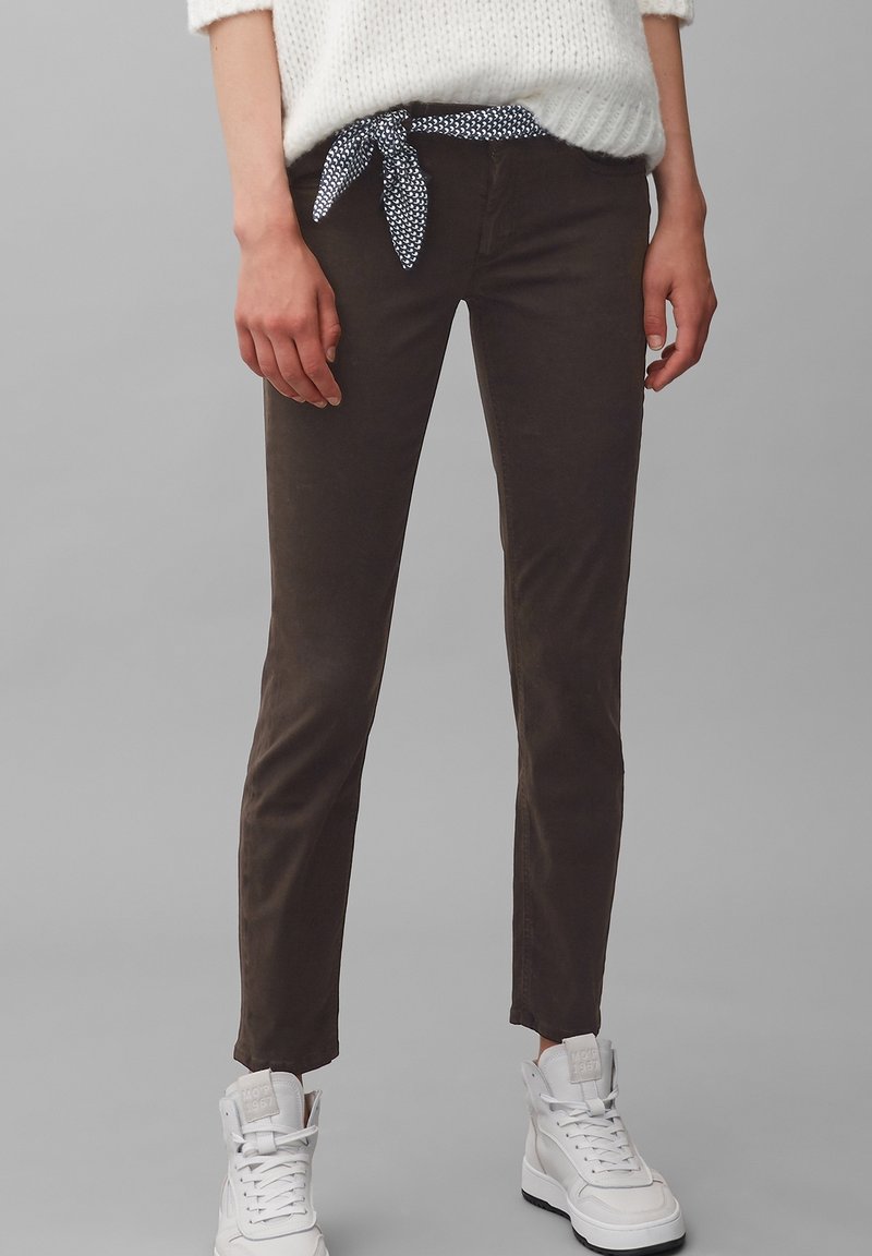 Pantaloni slanci marroni realizzati in materiale morbido, con una cintura a nodo blu navy con pois, abbinati a sneakers alte bianche.