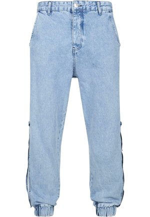 Joggers en denim bleu clair avec une coupe décontractée, poignets élastiques, poches latérales et fermeture à bouton. Présente des zip latéraux exposés.