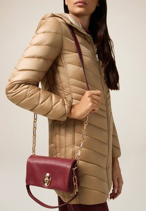 Doudoune beige avec capuche, présentant une texture matelassée. Un petit sac à bandoulière bordeaux avec une chaînette et des détails en doré.