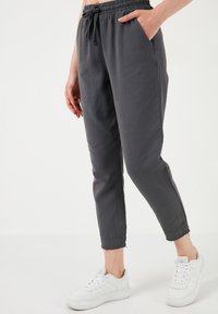 Grijze katoenen joggerbroek van een katoenmix met een elastische tailleband, zijzakken en taps toelopende enkels, gecombineerd met witte sneakers.