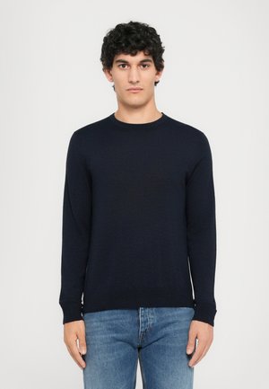 Pull à col rond marine foncé en tricot doux, avec des manches longues et un ourlet ajusté, associé à un jean en denim bleu clair.