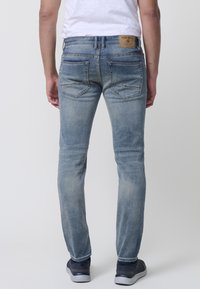 Világoskék farmernadrág slim fit fazonnal, elhasználódott textúrával, steppelt hátsó zsebekkel és márkás bőrpírral a derékrészen.
