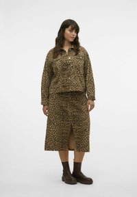 Leopardenmuster-Denimjacke mit Druckknöpfen, kombiniert mit einem passenden Rock mit einem Schlitz vorne. Braune Knöchelstiefel runden das Outfit ab.