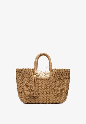 Woven straw tote bag with rounded handles, beige fabric drawstring pouch inside, and decorative tassel with wooden beads hanging by handle.