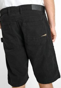 Zwarte cargoshorts met meerdere zakken, een gestructureerde stof en een tailleband met een logopatch. Het ontwerp is praktisch en functioneel.