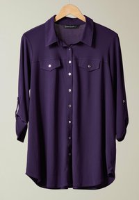 Purple button-up shirt with long sleeves, two chest pockets, silver buttons, and roll-tab cuffs. Smooth fabric with a relaxed fit.
