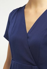 Marinblå omslagsklänning med korta ärmar, v-ringning och slätt, texturerat tyg, med en figursydd bodice och rynkad midjedetalj.