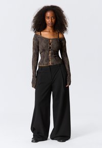 Black and brown patterned long-sleeve shirt with buttons down the front, paired with loose black trousers and flat shoes.