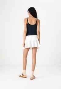 Débardeur marin, jupe blanche évasée, baskets à motifs avec des accents beiges, et chaussettes légères. Accent sur le matériau et les couleurs contrastantes.