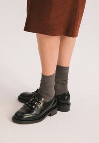 Scarpe stringate in pelle nera con punta arrotondata, caratterizzate da una finitura liscia e tacco basso a blocco, abbinate a calze grigie a coste.