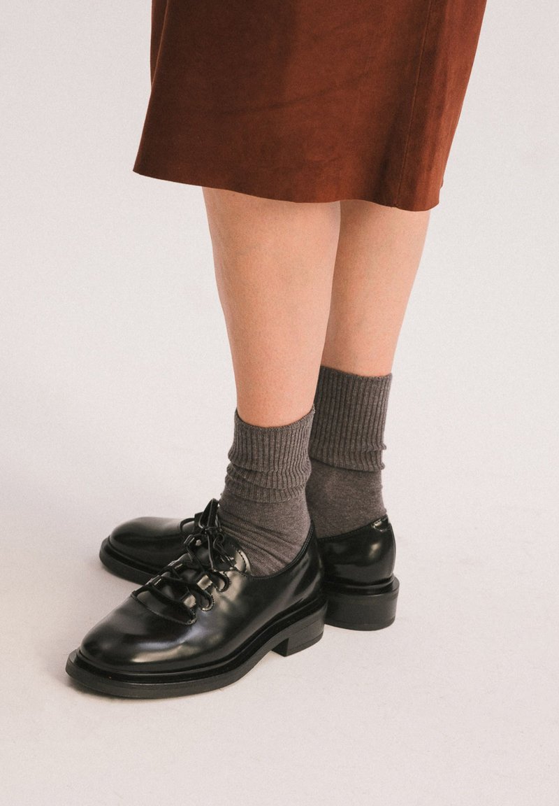 Scarpe stringate in pelle nera con punta arrotondata, caratterizzate da una finitura liscia e tacco basso a blocco, abbinate a calze grigie a coste.