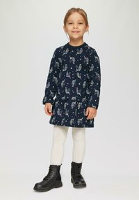 Marineblaues Kleid mit Einhorn- und Sternenmotiv, langen Ärmeln, gestuftem Design, kombiniert mit weißen Strumpfhosen und schwarzen Schnürstiefeln.