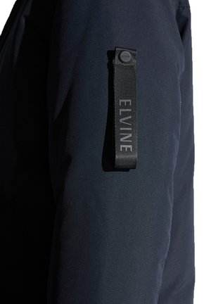 Mörkblå jacka med en slät tygstruktur och ett framträdande svart band med varumärke på ärmen, vilket ger en modern designdetalj.