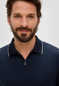 Granatowa koszulka polo na zamek z białym kołnierzykiem. Miękka tekstura materiału z dopasowanym krojem i minimalnymi detalami.