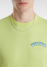 Lime green lyhythihainen T-paita, joka on valmistettu puuvillasta ja jossa on vasemmassa rintavarusteessa sininen "VANS" -logo. Sileä rakenne, pyöreä kaula-aukko.