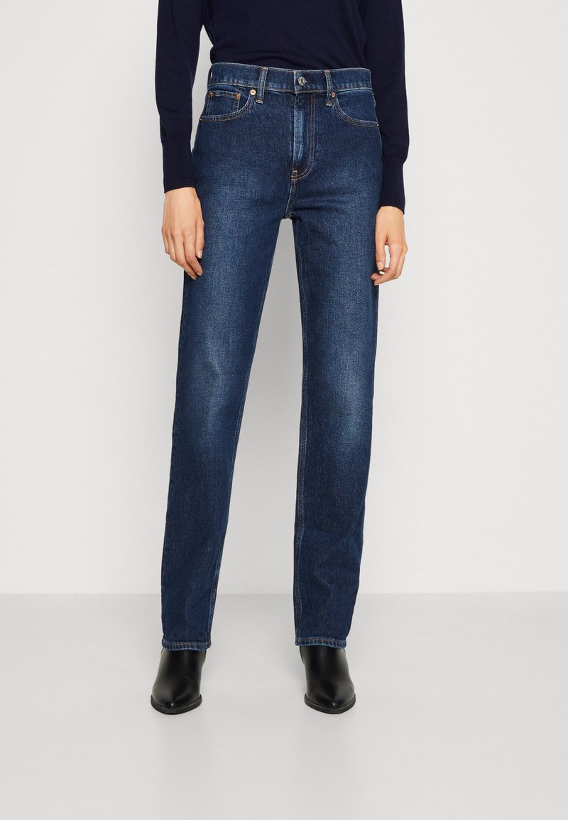 Tmavě modré džíny z denimu se střihem rovného nohavice, pěti kapsami a zapínáním na knoflík. Mají minimalistické prošití a klasický design.