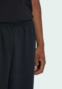 Black jogger pants with an elastic waistband, soft fabric texture, and side pockets, paired with a matching t-shirt. Hand resting on pants.