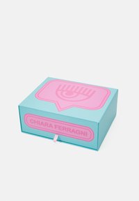 Tyrkysová krabička s růžovou grafikou oka a štítkem s nápisem "CHIARA FERRAGNI." Obsahuje vysouvací mechanismus a stuhový úchyt.