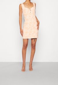 Brzoskwiniowa sukienka w kwiatowy wzór o dopasowanym kroju, kwadratowym dekolcie i trzech guzikach z przodu. Bez rękawów, gładka w dotyku.