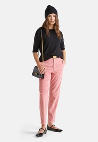 Czarna dzianinowa czapka, czarny bluzka z krótkim rękawem, różowe spodnie z korduroju, czarna torebka na ramię z złotymi elementami, oraz czarne płaskie buty.