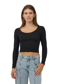 Czarny, krótki top z długim rękawem z okrągłym dekoltem, wykonany z gładkiej tkaniny. Połączony z jasnoniebieskimi dżinsami z wysokim stanem z przetarciami.