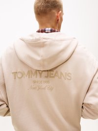 Felpa beige chiaro con vestibilità rilassata, caratterizzata da un logo testurizzato "TOMMY JEANS" e "New York City" stampato sul retro.