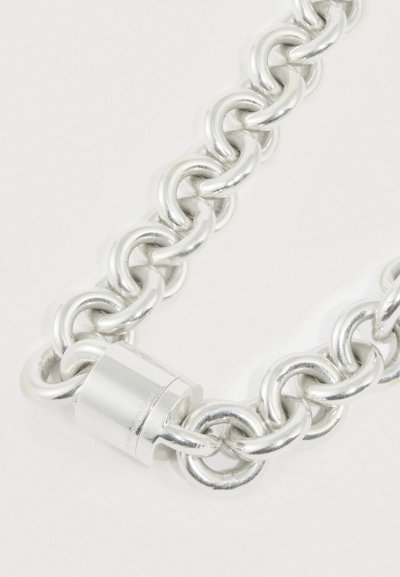 Kraftig sølvmetalkæde med store sammenflettede led, indeholder en cylindrisk lås som lukning, glat tekstur og poleret finish.