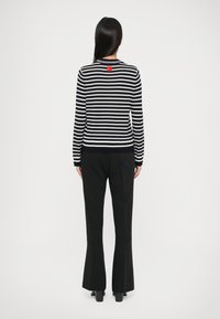 Maglione rigato blu navy e bianco con etichetta rossa sul retro, abbinato a pantaloni neri a zampa d'elefante. Tessuto morbido con maniche lunghe e colletto rotondo.