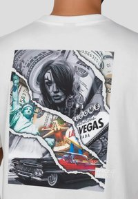 Hvid t-shirt med et flerfarvet grafisk motiv, der inkluderer billeder af frihedsgudinden, casinoelementer og vintagebiler i et revet design.