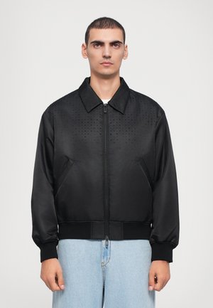 Schwarze Bomberjacke mit Reißverschluss vorne, strukturiertem Punktemuster an der Oberseite, elastischen Bündchen und Saum; aus glattem, leichtem Stoff gefertigt.