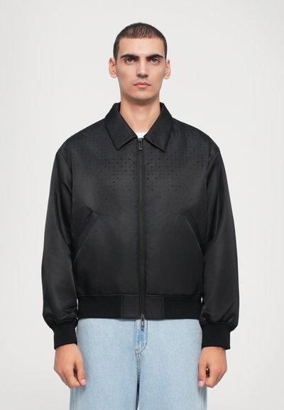 Veste bomber noire avec fermeture éclair à l'avant, motif en pointillés texturé sur le haut, poignets élastiques et ourlet ; fabriquée en tissu lisse et léger.